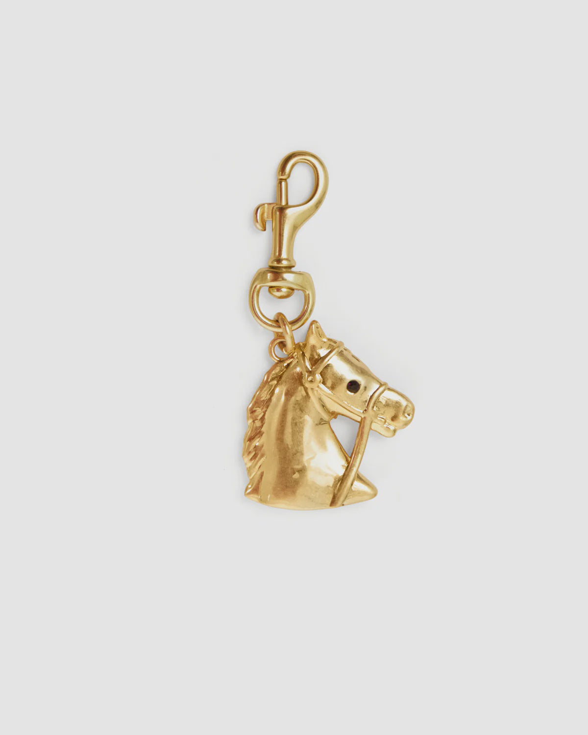The Le Cheval Fob by Clare Vivier is a vintage gold-plated brass keychain with a detailed horse head charm and bridle, attached to a swivel clasp, shown on a plain white background.