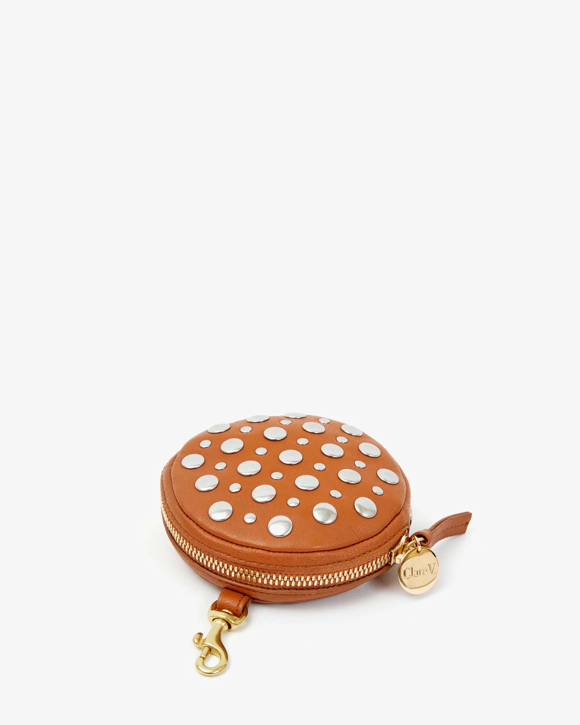 The Le Disco by Clare Vivier is a round, brown studded nappa leather pouch with a zipper, detailed with silver polka dots. It includes a gold clasp and a small gold charm featuring the text "Clare V," making it an ideal choice to infuse some disco flair into your outfit.