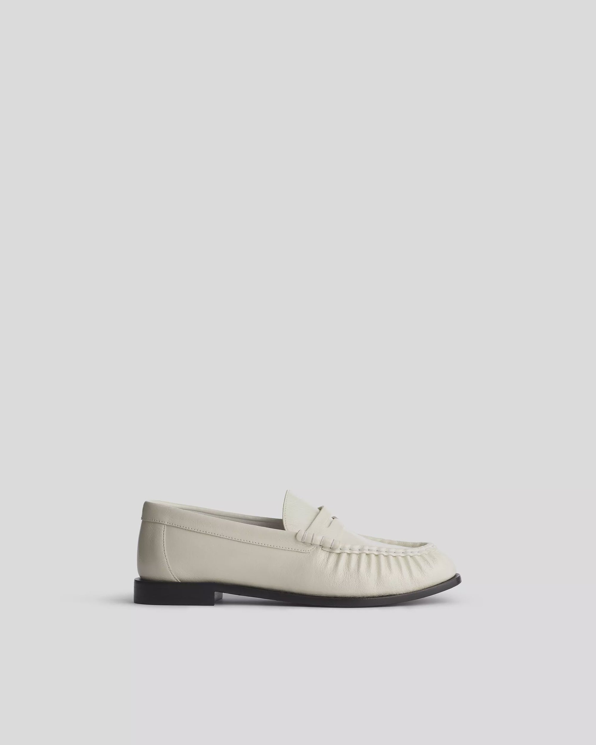The Rag & Bone Lexi loafer is an off-white slip-on with a moccasin-style toe, black sole, and OrthoLite foam insole for comfort, shown in profile on a plain light background.