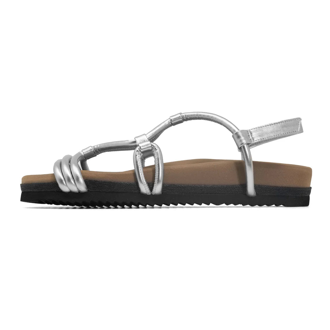 The Roam Linky Sandal by Roam features silver straps, a contoured footbed, flat tan base, and a black ridged sole made of sustainable BIO EVA, shown in profile view facing left.