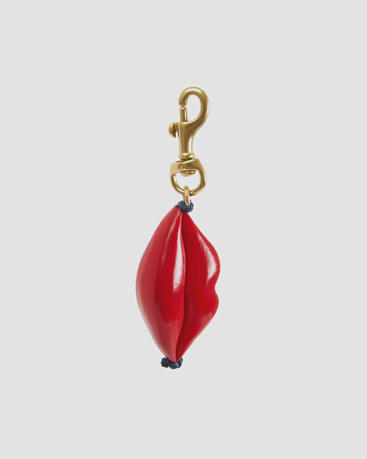 The Lips FOB by Clare Vivier is a vintage-inspired keychain featuring a 14k gold-plated brass hook attached to glossy red lips, connected with small black loops against a plain gray background.