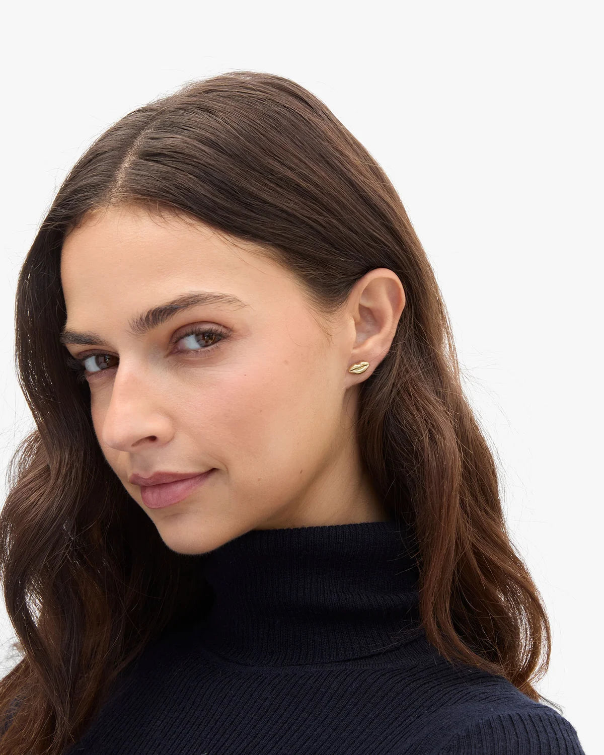 Clare Vivier Lips Stud Earrings in gold worn by woman with long brown hair and black turtleneck, casual chic style.