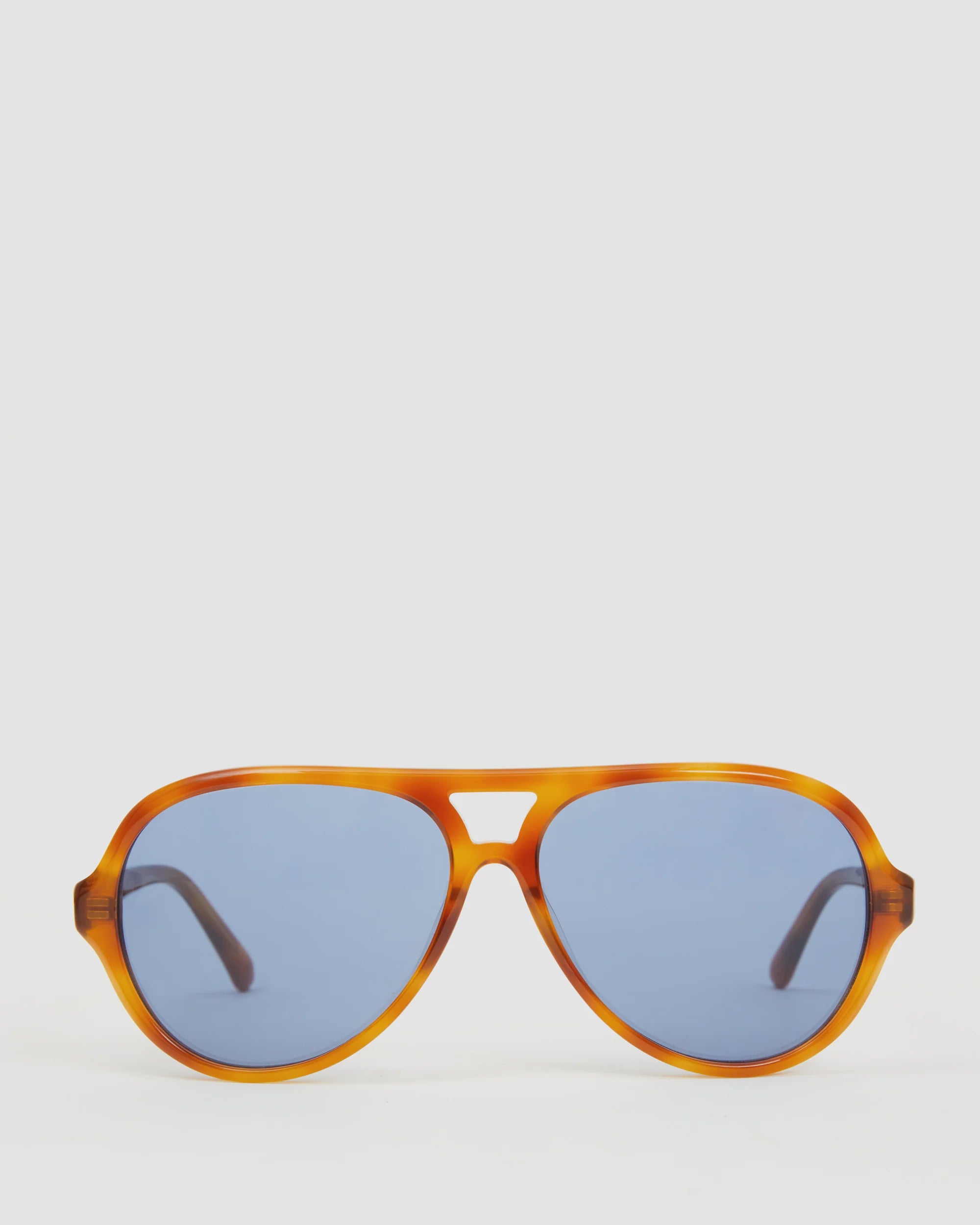 The Lizzie Sunglasses by Clare Vivier are a stylish pair of aviator sunglasses made from recycled bio-based materials, showcasing amber-colored frames and blue-tinted lenses, and providing 100% UVA/UVB protection against a plain white background.