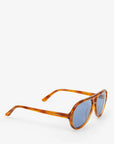 The Lizzie Sunglasses, designed by Clare Vivier, are showcased on a white background. Made from recycled bio-based materials, these environmentally friendly sunglasses come in a brown tortoiseshell frame with blue-tinted lenses. The arm features the brand name "CÉLINE V." and provides essential UVA/UVB protection.