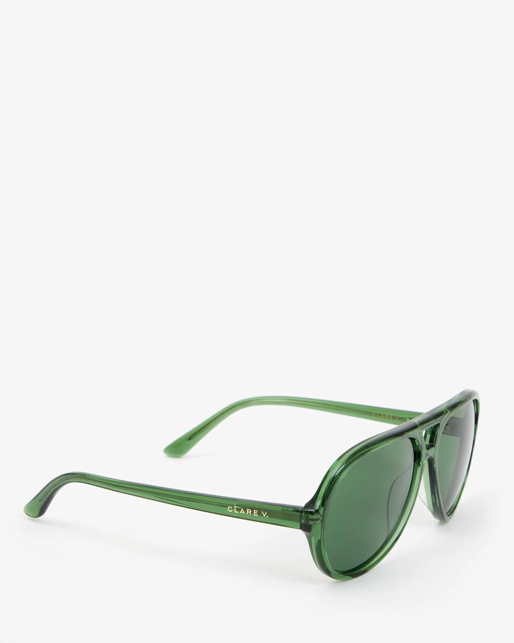 Lizzie Sunglasses by Clare Vivier feature green oval lenses set in a translucent frame and are shown angled on a plain white background. Made from recycled bio-based materials, the arms bear &quot;Clare V.&quot; in gold near the hinges, offering both style and UVA/UVB protection for your eyes.