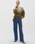 A woman stands against a white background wearing Rag & Bone ftwt logan mr wide leg jeans in dark indigo, paired with a fuzzy patterned sweater in olive green, white, and beige, and dark pointed-toe boots.