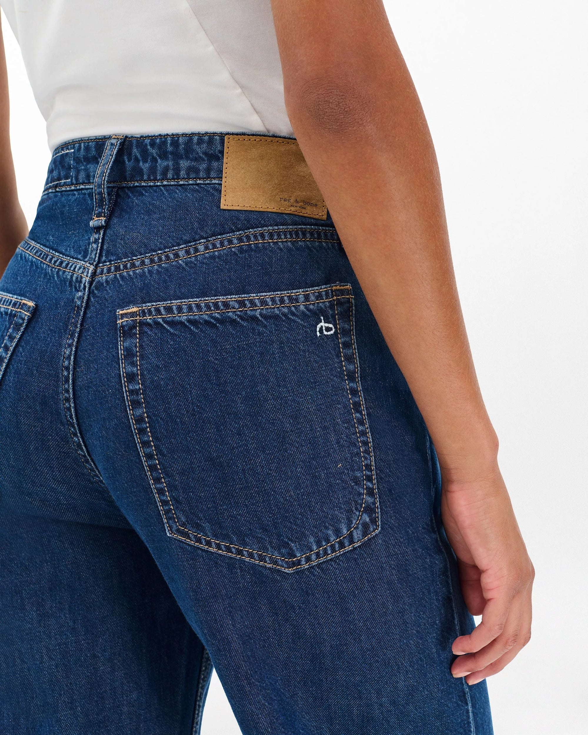Someone is shown from the back wearing Rag & Bone ftwt logan mr wide leg high-waisted dark indigo jeans with visible back pockets and a brown leather patch on the waistband, paired with a partially visible white shirt.