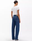 A person with dark hair in a bun faces away, wearing a fitted white tee and Rag & Bone ftwt logan mr wide leg jeans in dark indigo, standing against a plain white background.