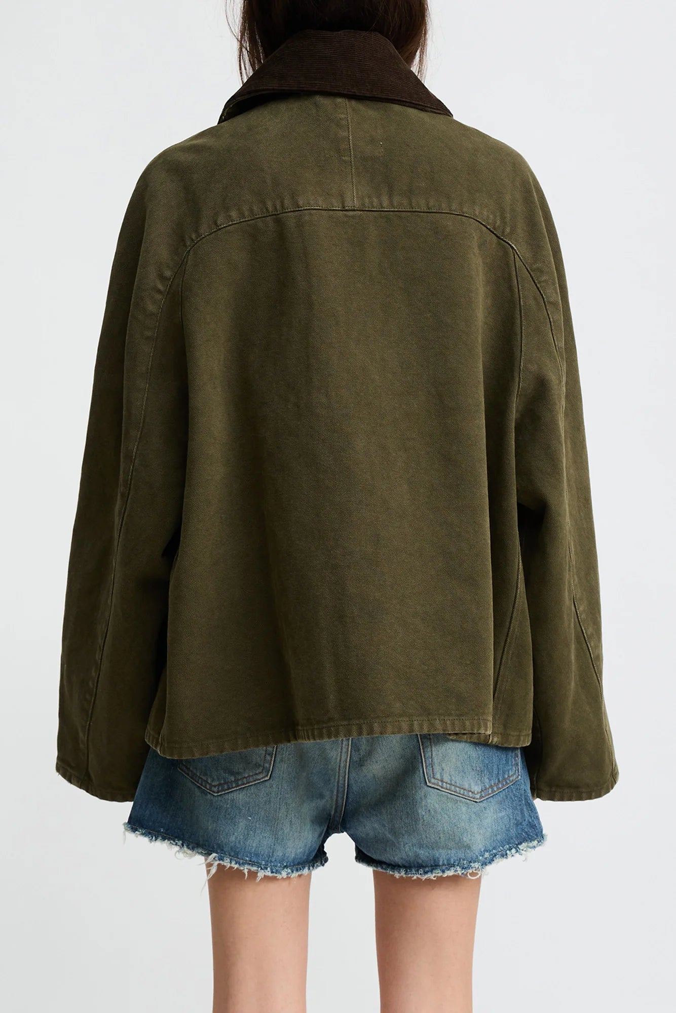 A person wearing the Denimist O/S Field Jacket in sturdy cotton with a dark collar and frayed blue denim shorts, shown from the back against a plain light background.