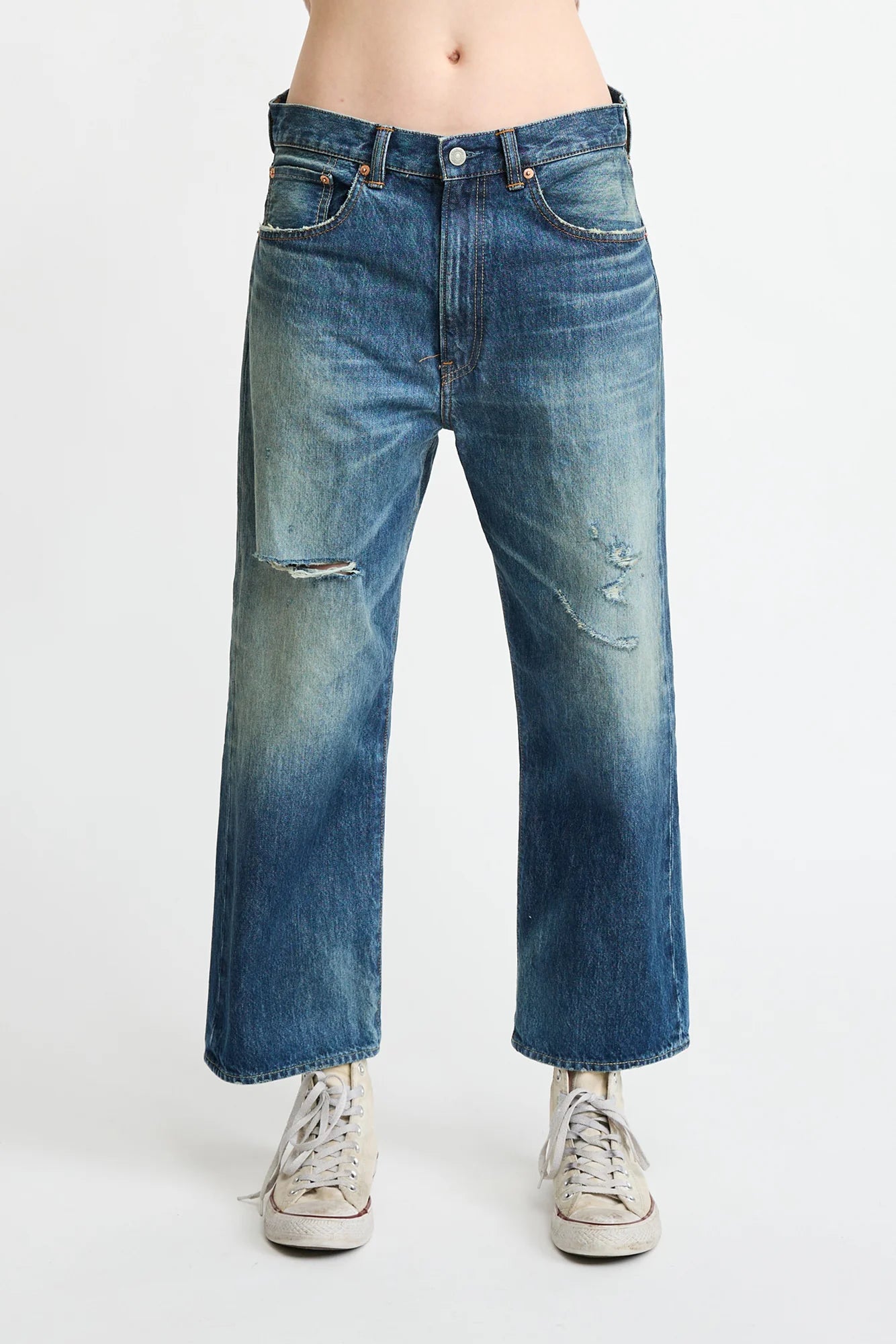 A person models Denimist’s HAISLEY SLOUCH BF JEAN—premium blue, mid-rise, straight-leg denim with light distressing—paired with white sneakers, standing against a plain white background. Upper body not visible.
