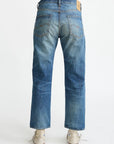 A person in Denimist LUCY BF JEAN ESHER BLUE, relaxed fit, and white sneakers stands facing away, showcasing the jeans’ two back pockets and leather patch on the waistband.