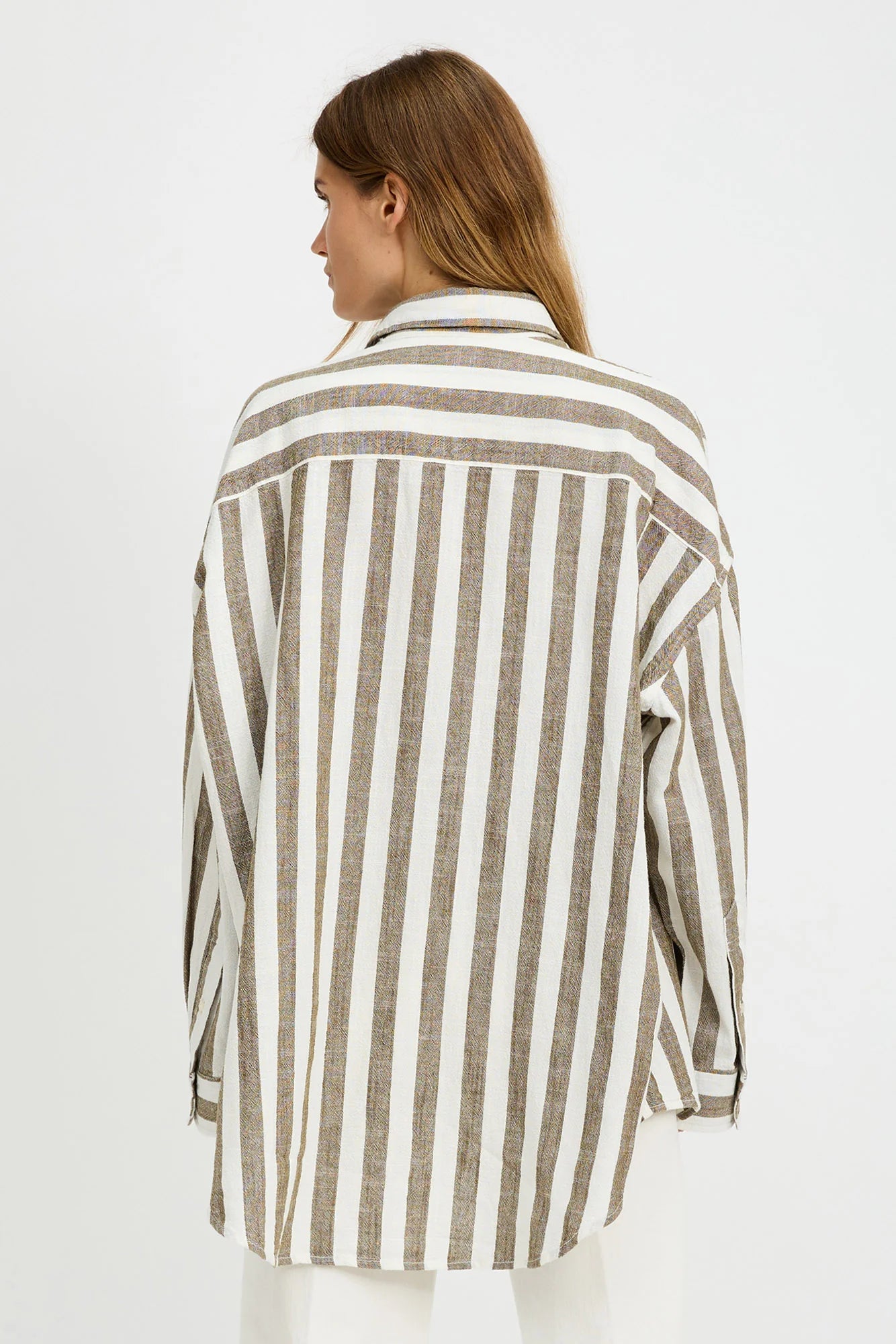 A woman with light brown hair stands with her back to the camera, wearing the Denimist BUTTON FRONT SHIRT STRIPE—a relaxed fit, long-sleeve shirt with jumbo beige and white stripes—against a plain white background.