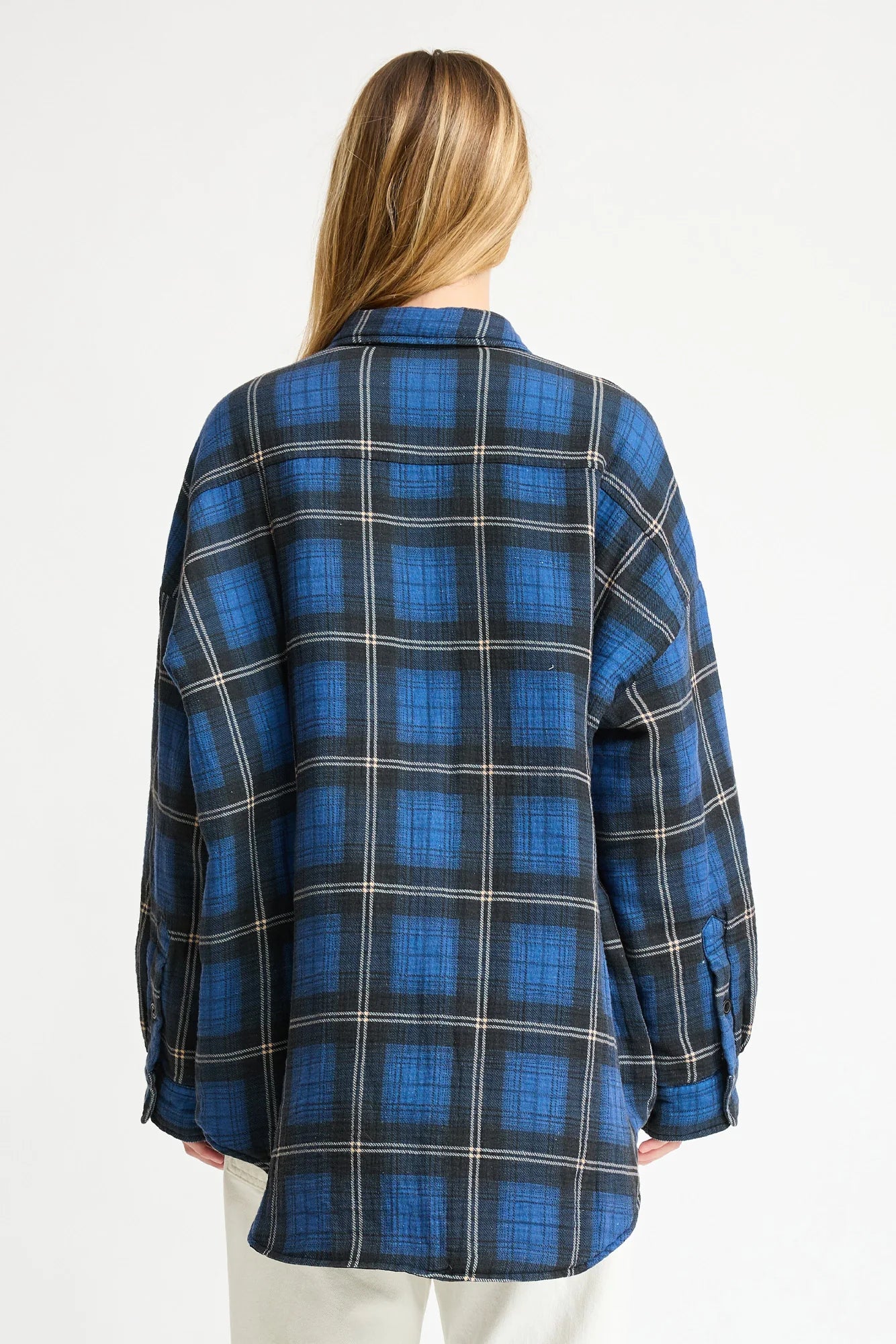 A person with long blonde hair is seen from the back, wearing a loose-fitting blue and black plaid Denimist CPO SHIRT JACKET against a plain white background.