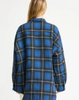 A person with long blonde hair is seen from the back, wearing a loose-fitting blue and black plaid Denimist CPO SHIRT JACKET against a plain white background.