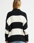 A person with long, light brown hair is seen from behind, wearing the Denimist OVERSIZED RIBBED SWEATER in black and white stripes and light blue jeans against a plain white background.