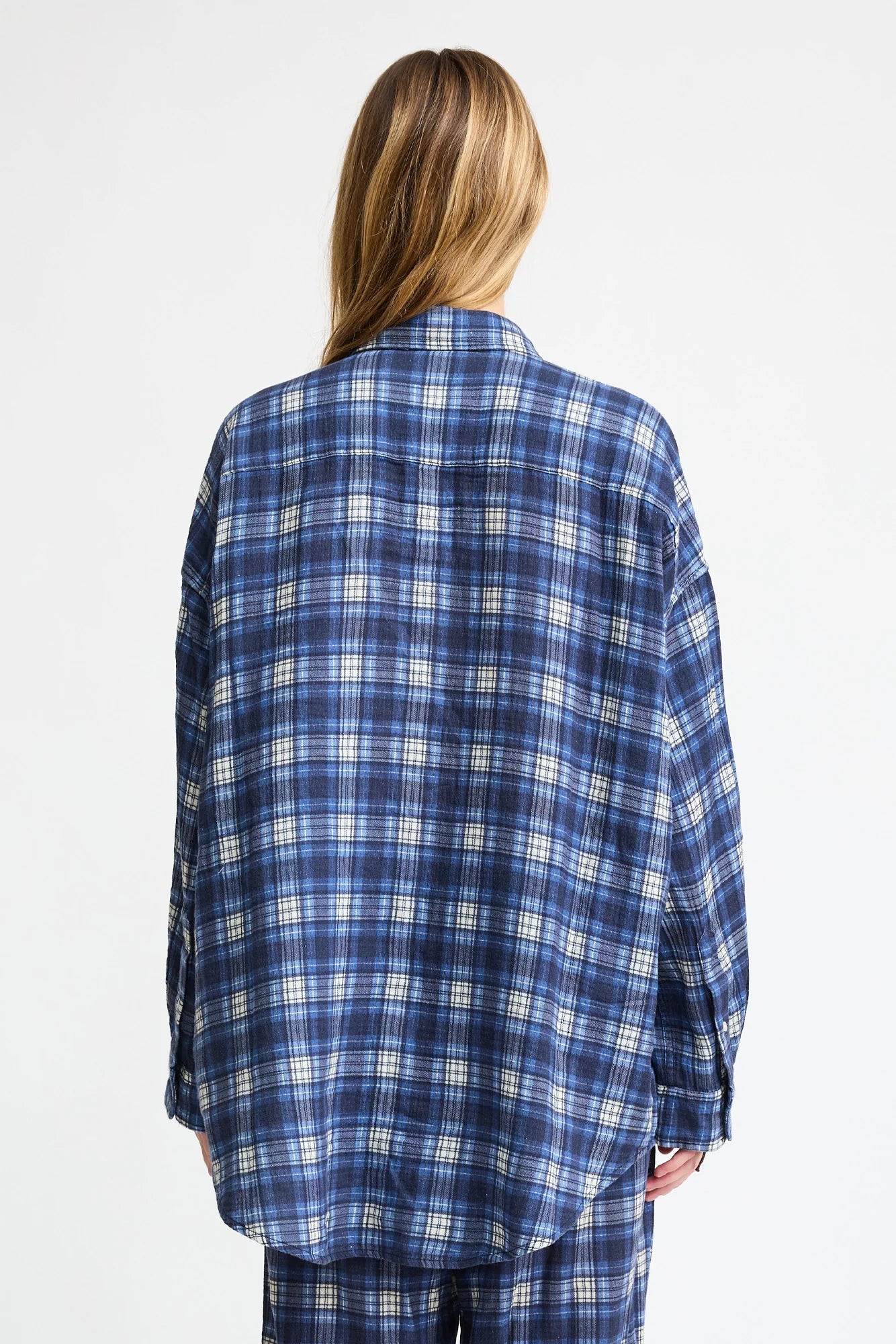 A person with long, light brown hair stands facing away from the camera, wearing the Denimist BUTTON FRONT SHIRT in blue/ecru plaid against a plain white background.