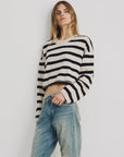 A person with long hair wears a Denimist CROPPED STRIPE SWEATER in black and white with loose, light blue ripped jeans, standing against a plain white background.