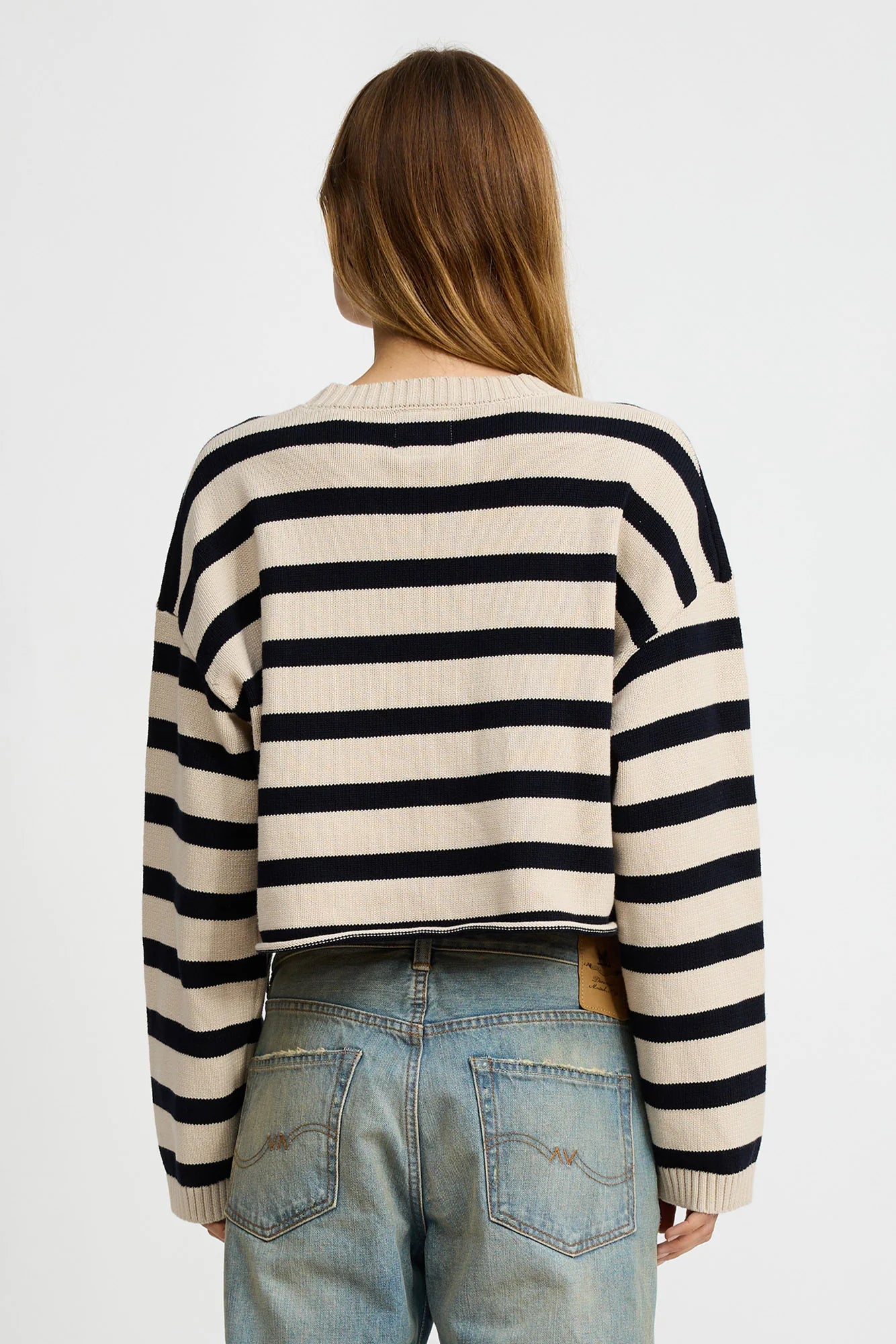 A person with long brown hair, seen from behind, wears the Denimist CROPPED STRIPE SWEATER with light blue jeans against a plain white background.