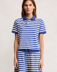 A woman faces forward in Denimist's SHRUNKEN POLO—a blue and white striped cotton polo t-shirt with matching drawstring shorts—posing against a neutral background.
