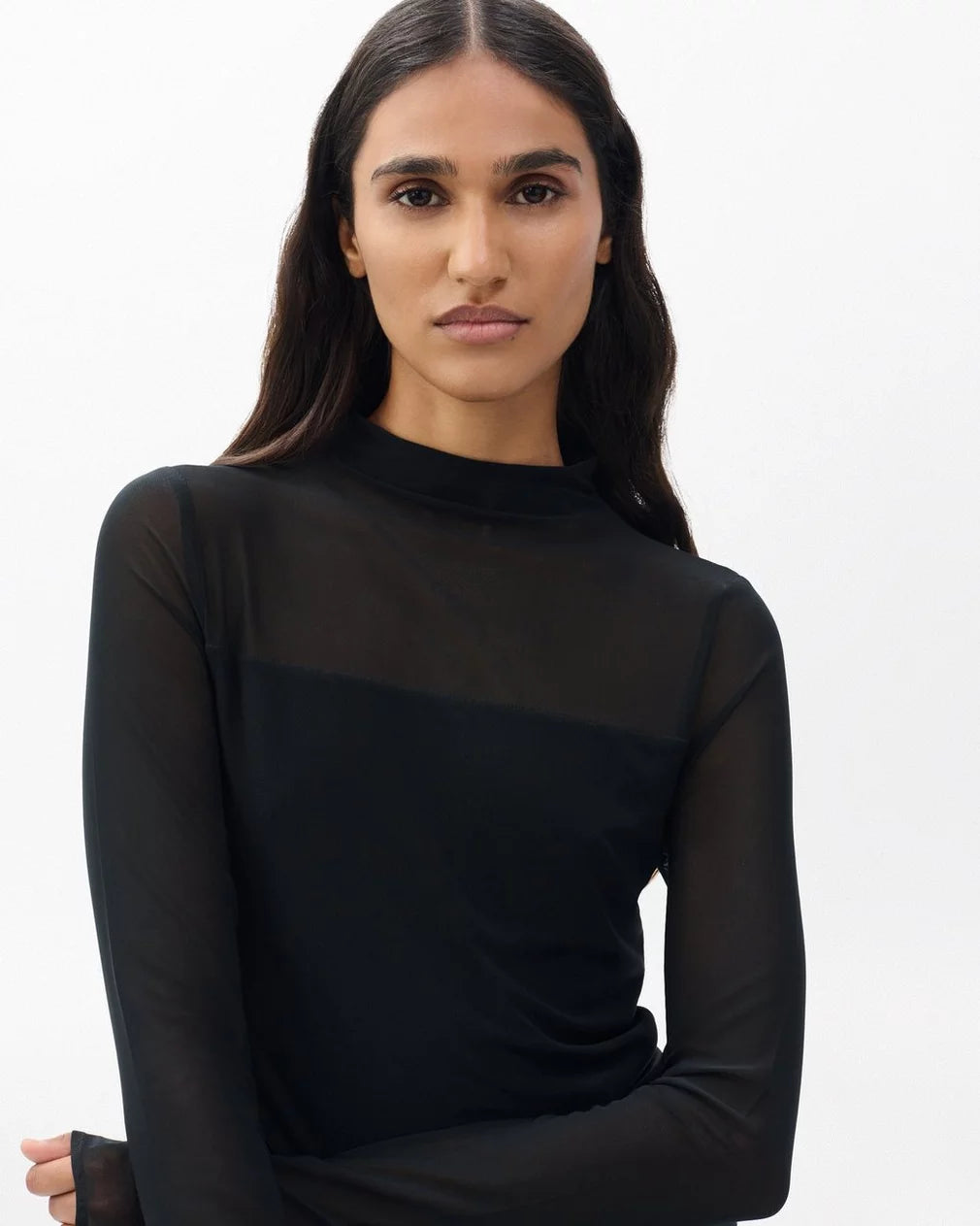 A woman with long dark hair models the Rag & Bone luca dbl layer mix media mockneck long-sleeve top in black, standing confidently against a plain white background.
