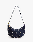 The Clare Vivier F25-Lune is a navy blue suede shoulder bag featuring a curved design, a knotted strap, and silver studs evenly spaced across the front.