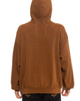 Someone wearing the Aviator Nation "locals only - pullover hoodie relaxed" in brown with the hood up, seen from behind. The unisex, loose-fit hoodie is paired with black pants featuring small embroidered designs on the back pockets.