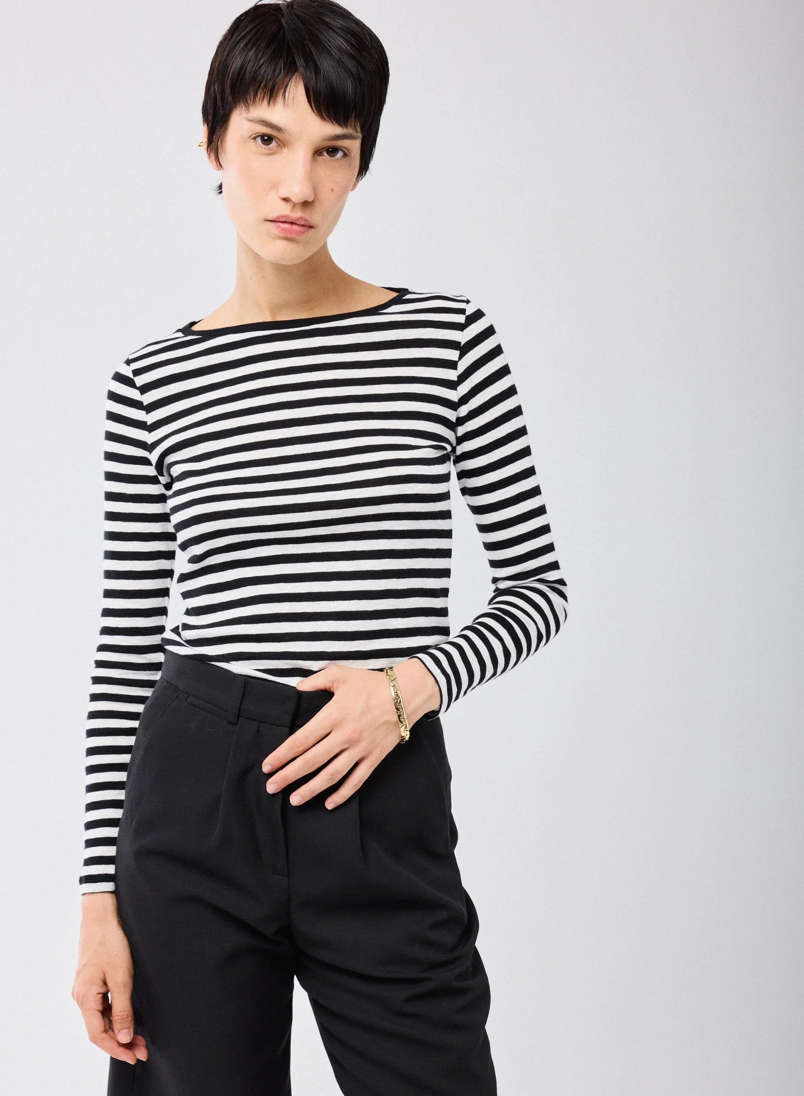A person with short dark hair wears the Majestic Filatures Organic Cotton Stripe L/S Crewneck and black pants, standing against a plain light background, looking at the camera with a neutral expression.