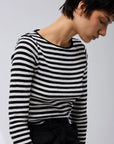 A person with short dark hair is seated against a plain light background, wearing the Majestic Filatures Organic Cotton Stripe L/S Crewneck and black pants.