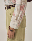 Wearing the Maison Hotel Narciso Shirt tucked into high-waisted light khaki cargo pants with a dark brown belt, accessorized with rings and a bracelet on the left hand.