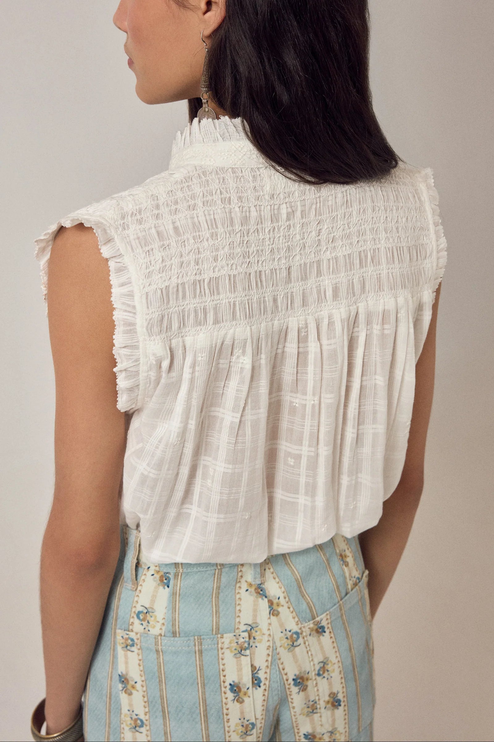 A woman with long dark hair is shown from the back wearing the Maison Hotel Elvis Sleeveless Blouse and high-waisted blue and white striped floral pants, set against a neutral background.