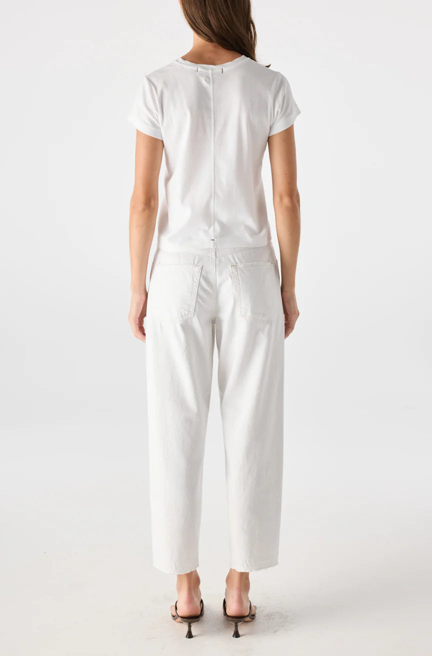 A woman faces away against a plain white background, wearing a white short-sleeve t-shirt, AMO Denim's Maria Denim vintage-inspired loose fit jeans, and black heeled sandals.