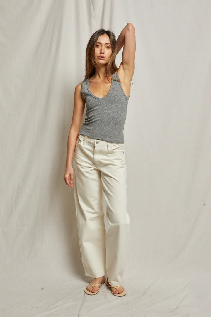 A woman poses against a plain backdrop wearing the Maria Rib V Tank by Perfectwhitetee in gray and white pants, one arm raised to her head. She has long hair and wears sandals.