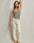 A woman poses against a plain backdrop wearing the Maria Rib V Tank by Perfectwhitetee in gray and white pants, one arm raised to her head. She has long hair and wears sandals.