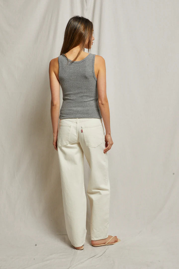 A woman with long hair stands with her back to the camera, wearing a Perfectwhitetee Maria Rib V Tank and gray and white pants. The background features plain, light-colored fabric.