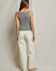 A woman with long hair stands with her back to the camera, wearing a Perfectwhitetee Maria Rib V Tank and gray and white pants. The background features plain, light-colored fabric.