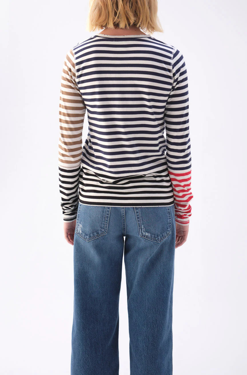 An individual with blonde hair faces away from the camera, donning blue jeans and the AMO Denim Marla Tee, a chic high-necked, long-sleeve shirt made of 100% cotton. It features stylish tri-color stripes in black, white, and red.