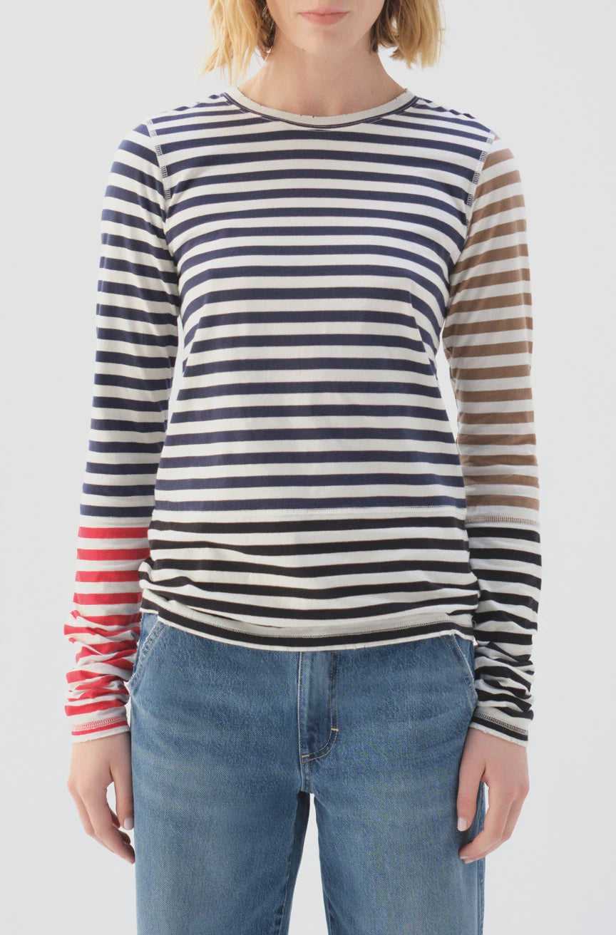 Someone wearing the Marla Tee by AMO Denim, featuring navy, beige, and red stripes with a high neckline in 100% cotton, is paired with blue jeans against a plain light-colored backdrop.