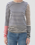 Someone wearing the Marla Tee by AMO Denim, featuring navy, beige, and red stripes with a high neckline in 100% cotton, is paired with blue jeans against a plain light-colored backdrop.