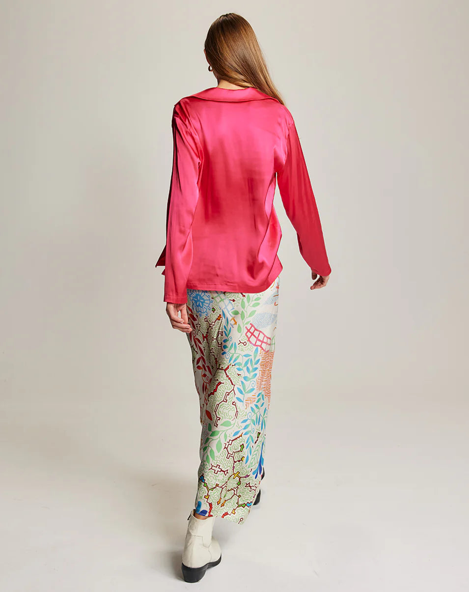 A woman with long hair, seen from behind in a neutral studio, wears a shiny pink blouse and the colorful Blakely Slip Skirt by Me369, featuring an elastic waist, paired with white boots.