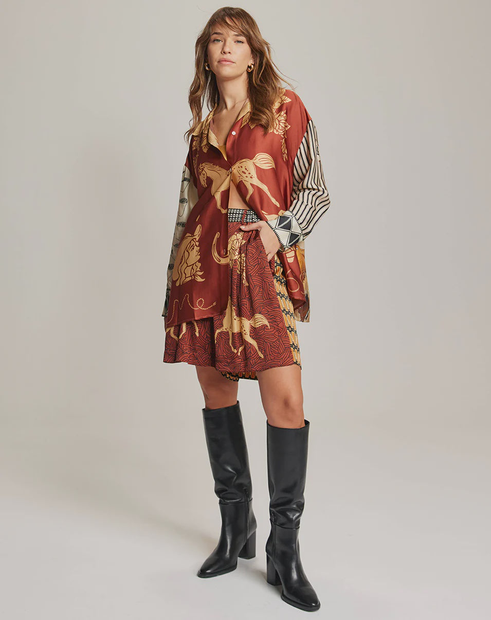 A woman poses in Me369's Juliette Pleated Shorts paired with black knee-high boots, standing against a plain background.