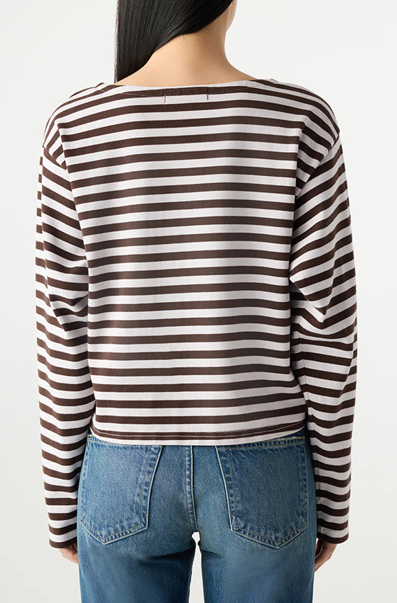 A person with long dark hair, seen from the back, wears the AMO Denim Hepburn Top— a relaxed fit brown and white striped heavyweight cotton long sleeve shirt—paired with blue jeans against a plain light background.