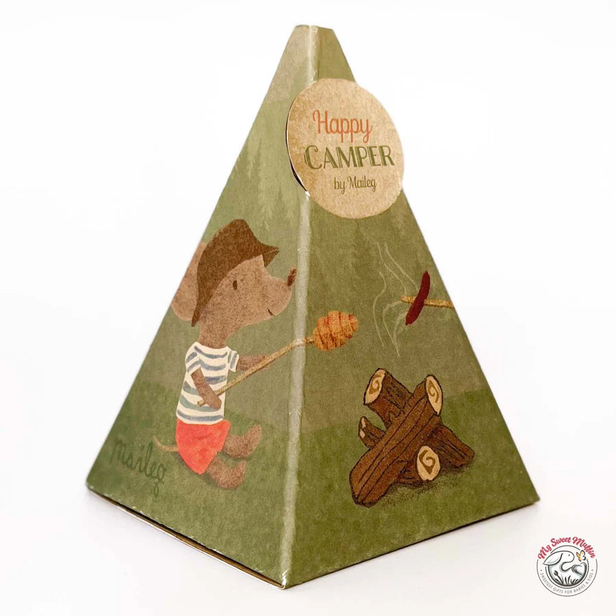 Pyramid-shaped box featuring a hiking mouse doll in a hat and shorts roasting marshmallows by the campfire. The circular label reads "Happy CAMPER by Mallory." The Maileg Bonfire Set by Maileg is perfect for mouse camping adventures.