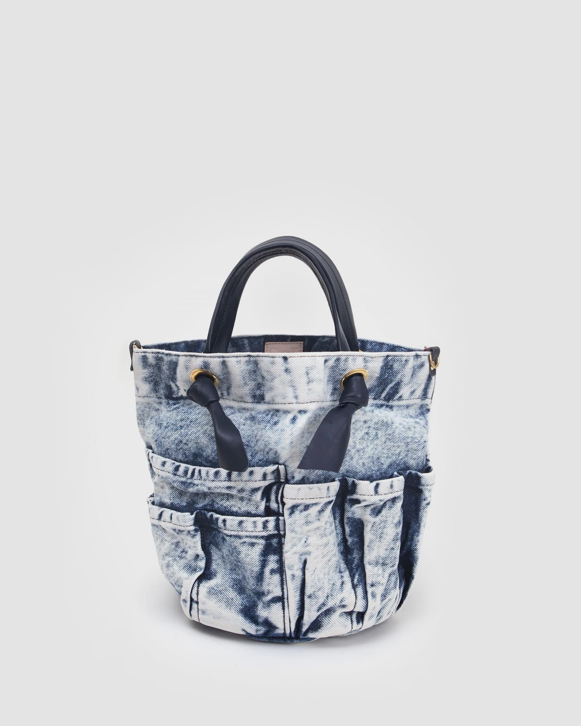 The Clare Vivier Marine Bag is crafted from blue acid-wash denim with multiple exterior pockets and two dark handles, shown against a plain white background.