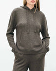 A woman stands with her hands in the pockets of a dark gray Jumper 1 2 3 4/CR2 Oversized Hoodie and matching pants against a light background. Her face is partially visible.