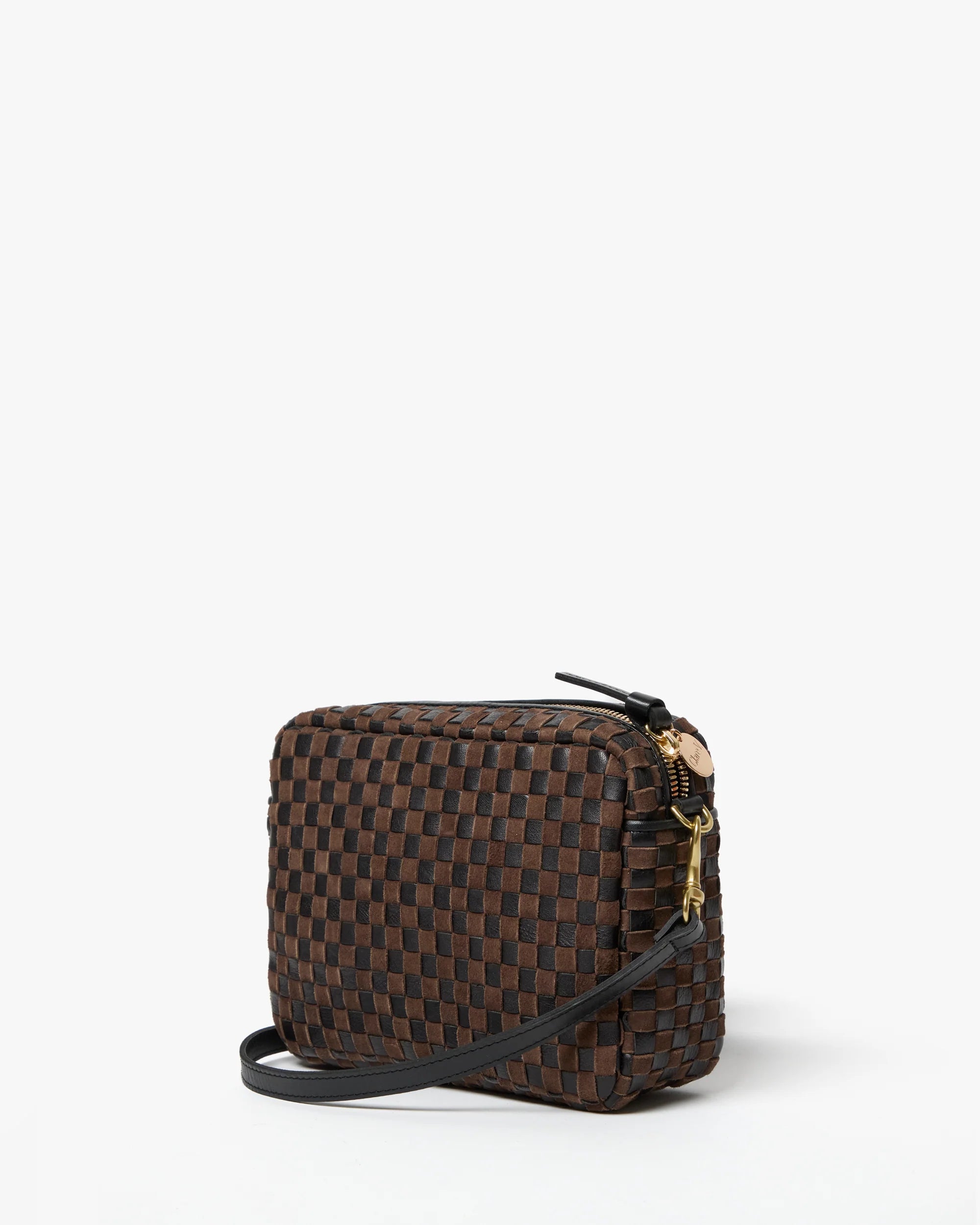 The Clare Vivier Midi Sac S25 is a small, square handwoven leather crossbody with a dark brown and black checkerboard pattern, black strap, and gold zipper hardware, displayed on a plain white background.