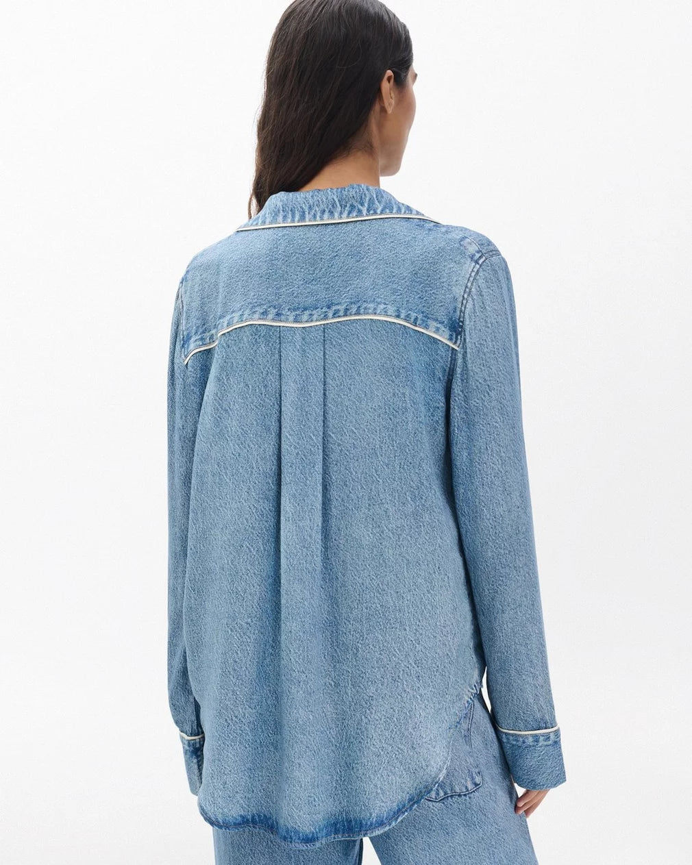A person with long dark hair is seen from behind, wearing the Rag & Bone miramar slink long sleeve lounge shirt in a light blue denim print, paired with matching pants, set against a plain white background.