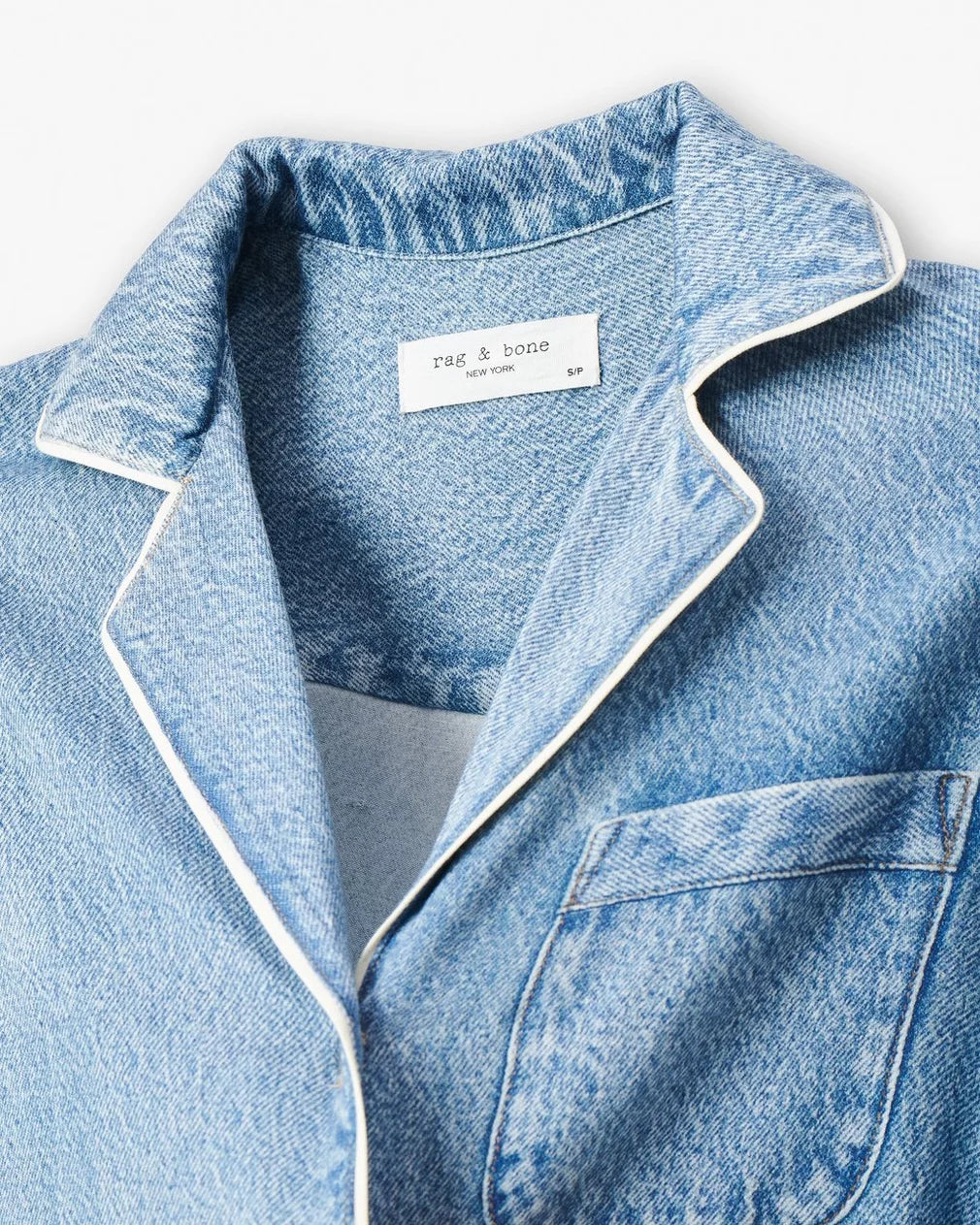 A close-up of the light blue Rag & Bone Miramar Slink Long Sleeve Lounge Shirt, featuring white piping on the collar and chest pocket. The inner label reads "rag & bone NEW YORK SP." Ideal for stylish, comfortable loungewear.