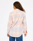 A person with long, curly hair is shown from the back wearing the Kerri Rosenthal Molly Shirt—a loose-fitting, long-sleeve plaid flannel—paired with blue jeans, against a plain white background.