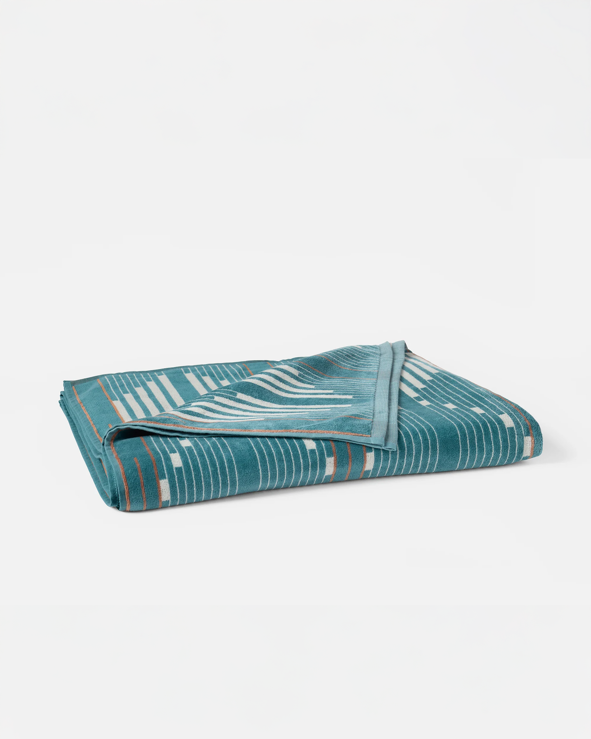 The Morelia Beach Towel by Coyuchi Inc, crafted in soft velour terry, features a teal organic fabric with a geometric pattern of white and light brown lines and rectangles. It is shown folded on a plain white background.