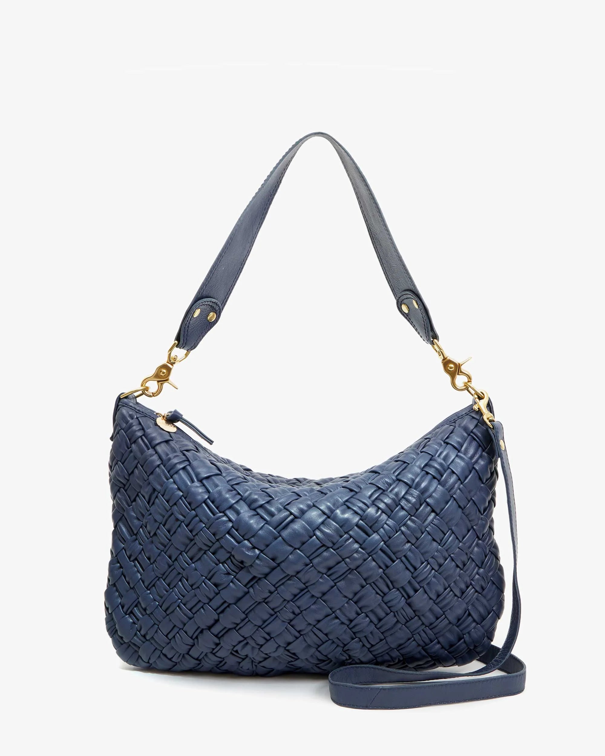 The Moyen Messenger by Clare Vivier is a navy blue nappa woven leather handbag featuring a short strap and gold hardware. Set against a plain background, this zip-top crescent bag highlights its intricate weaving, combining elegance with versatility.